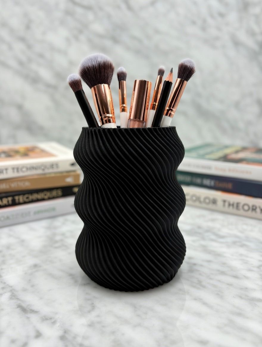 Black wavy twisted pencil holder on a desk with postcards and supplies
